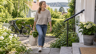 Kvinna som bär en matkasse uppför trappor med en cykel i bakgrunden